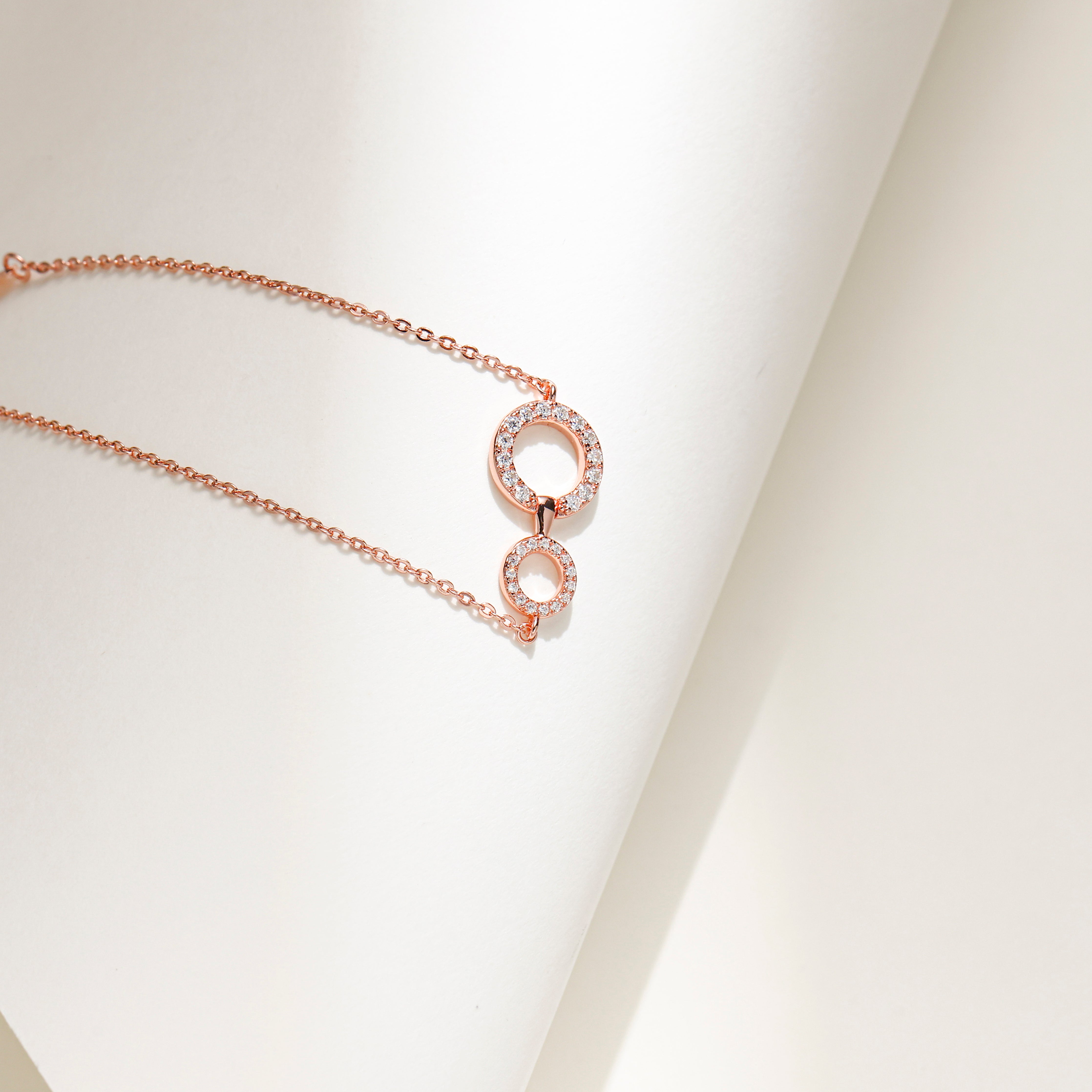 Elegant rose gold plated sterling silver bracelet featuring two interlinked circles adorned with sparkling Moissanite stones and an adjustable chain.