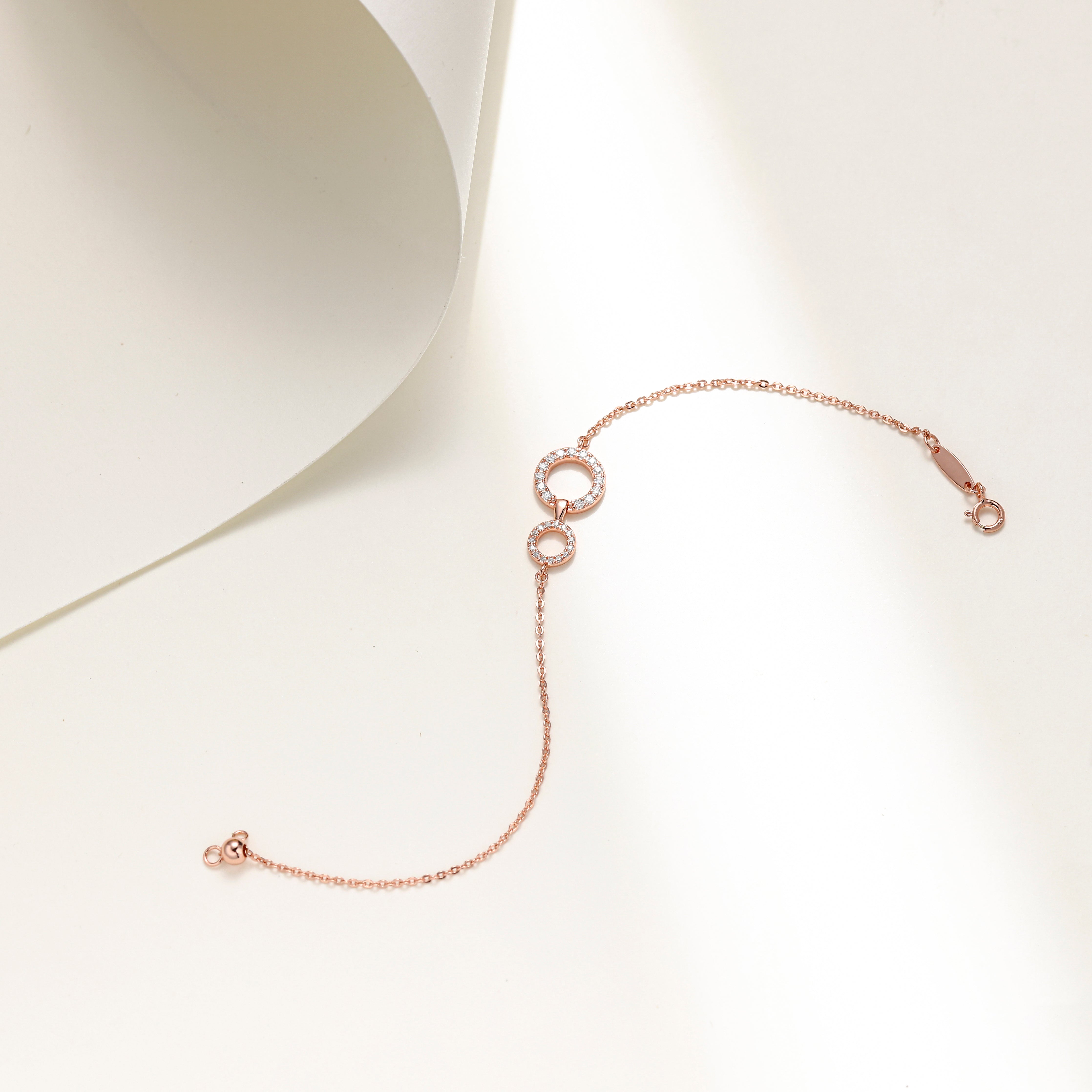 Elegant rose gold plated sterling silver bracelet featuring two interlinked circles adorned with sparkling Moissanite stones and an adjustable chain.