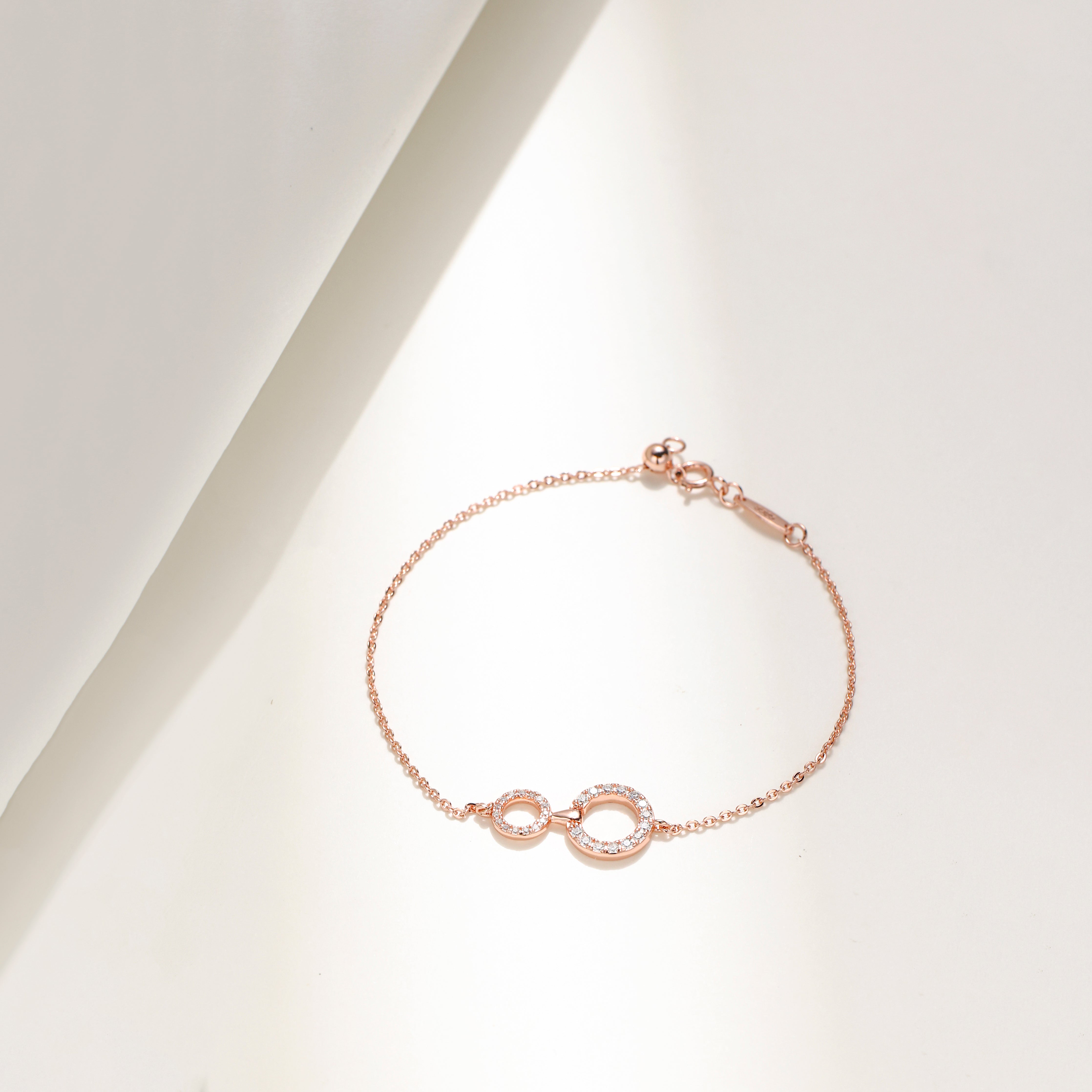 Elegant rose gold plated sterling silver bracelet featuring two interlinked circles adorned with sparkling Moissanite stones and an adjustable chain.