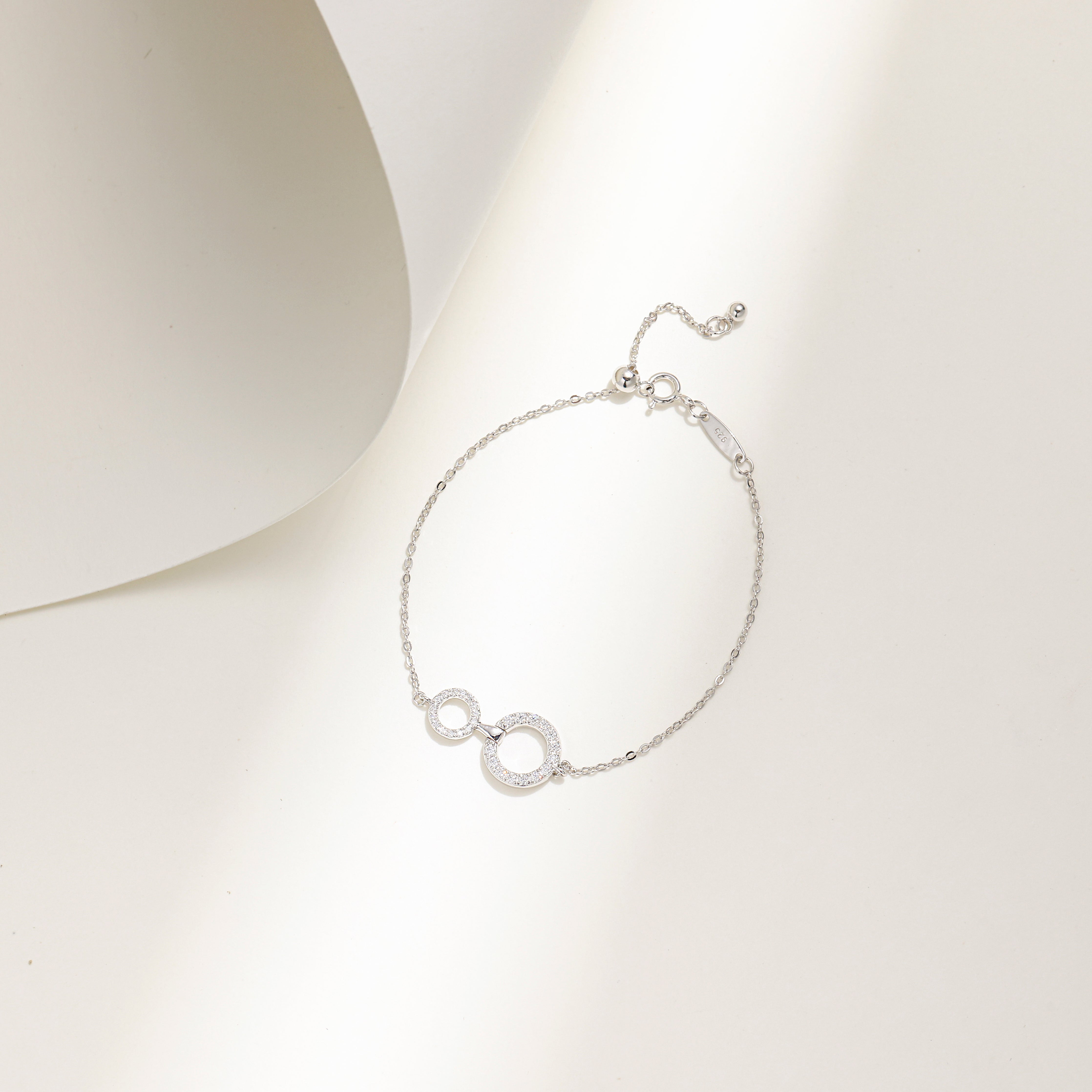 Elegant white gold plated sterling silver bracelet featuring two interlinked circles adorned with sparkling Moissanite stones and an adjustable chain.